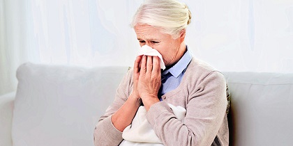 Image of a lady with a flu blowing her nose with a tissue